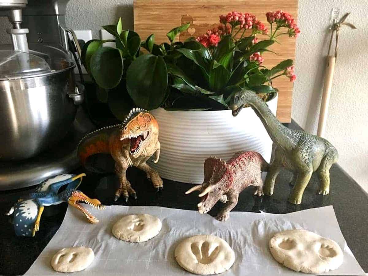 Dinosaur toys and clay fossil footprints drying on parchment paper for Montessori Geology & Paleontology Unit Study