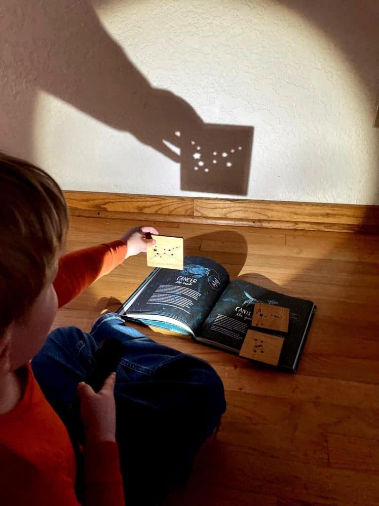 a child holding up a constellation tile to a flashlight