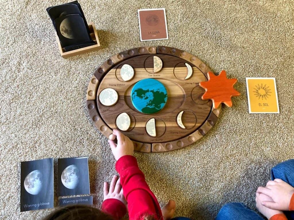 children sitting on a floor with language materials and a moon phases puzzle