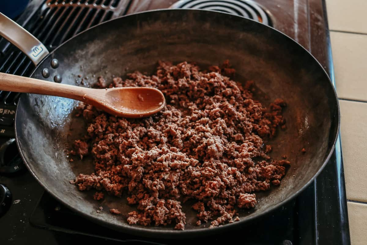 ground beef in a carbon steel pan with a wooden spoon