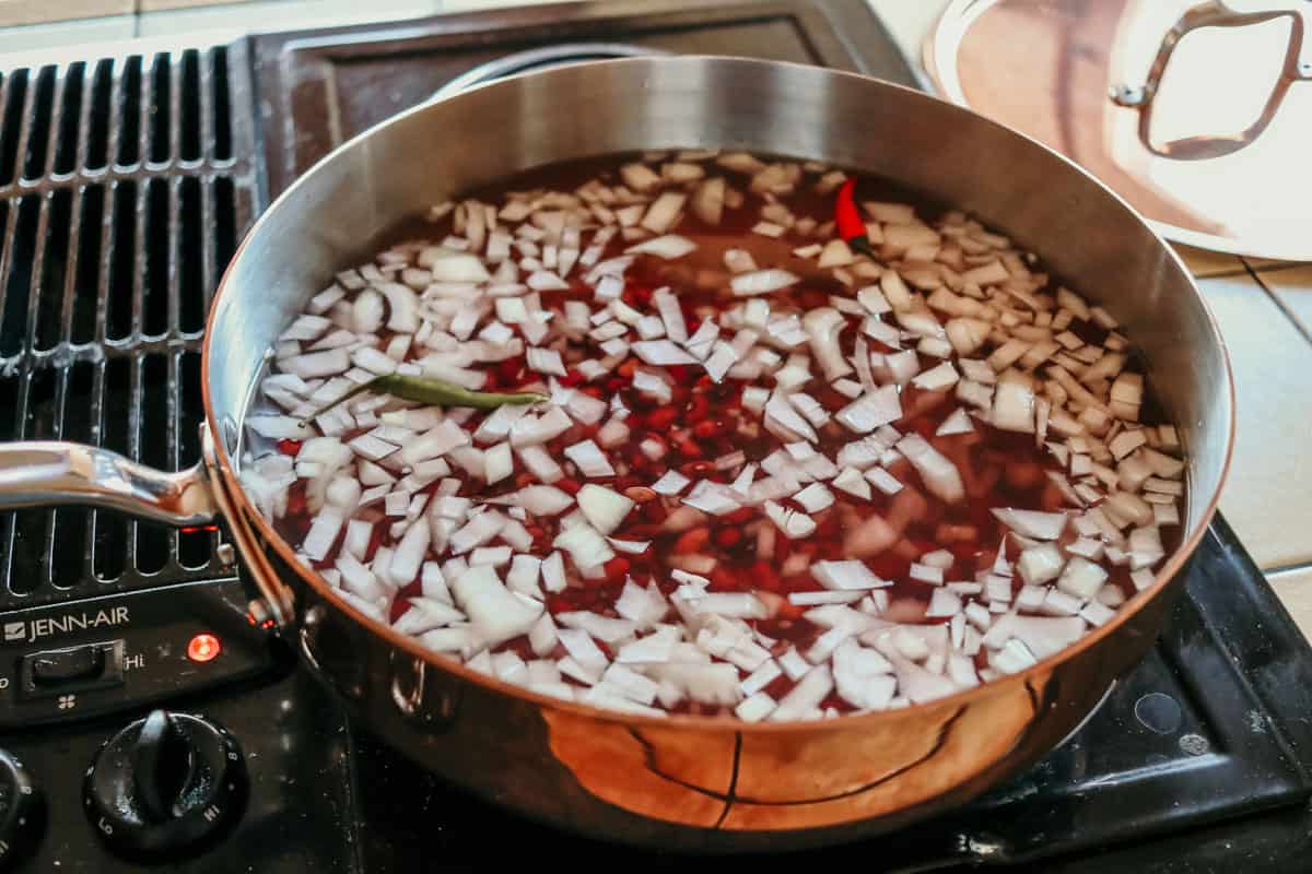 red beans, onions, bird's eye chiles and other ingredients cooking in a copper saucier