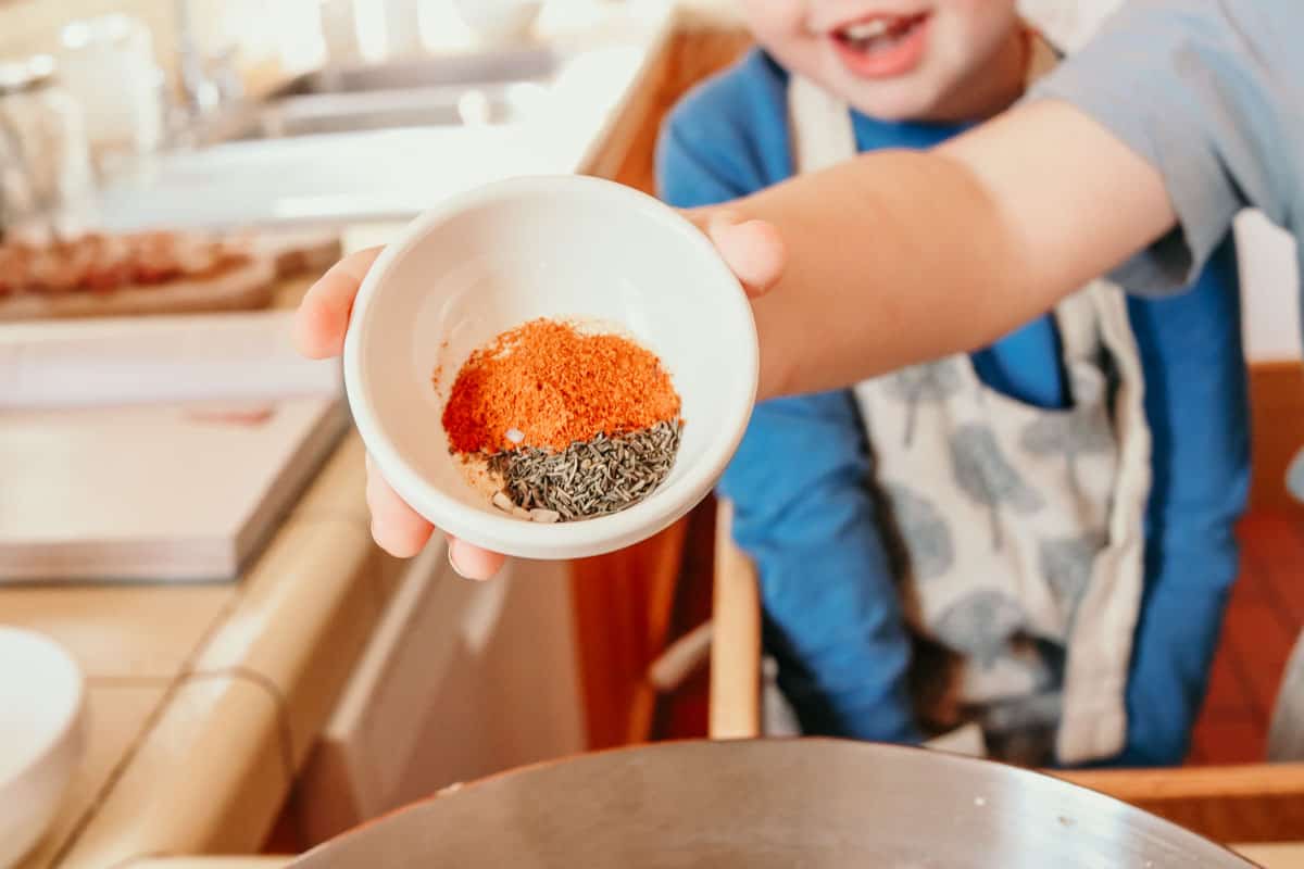 child adding colorful spices to a saucier