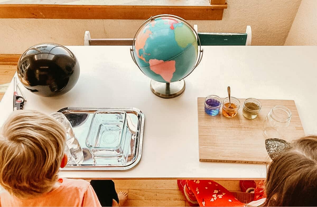 Montessori Kids sitting at table with items for History of the Universe The First Great Lesson and Laws of the Universe Experiments