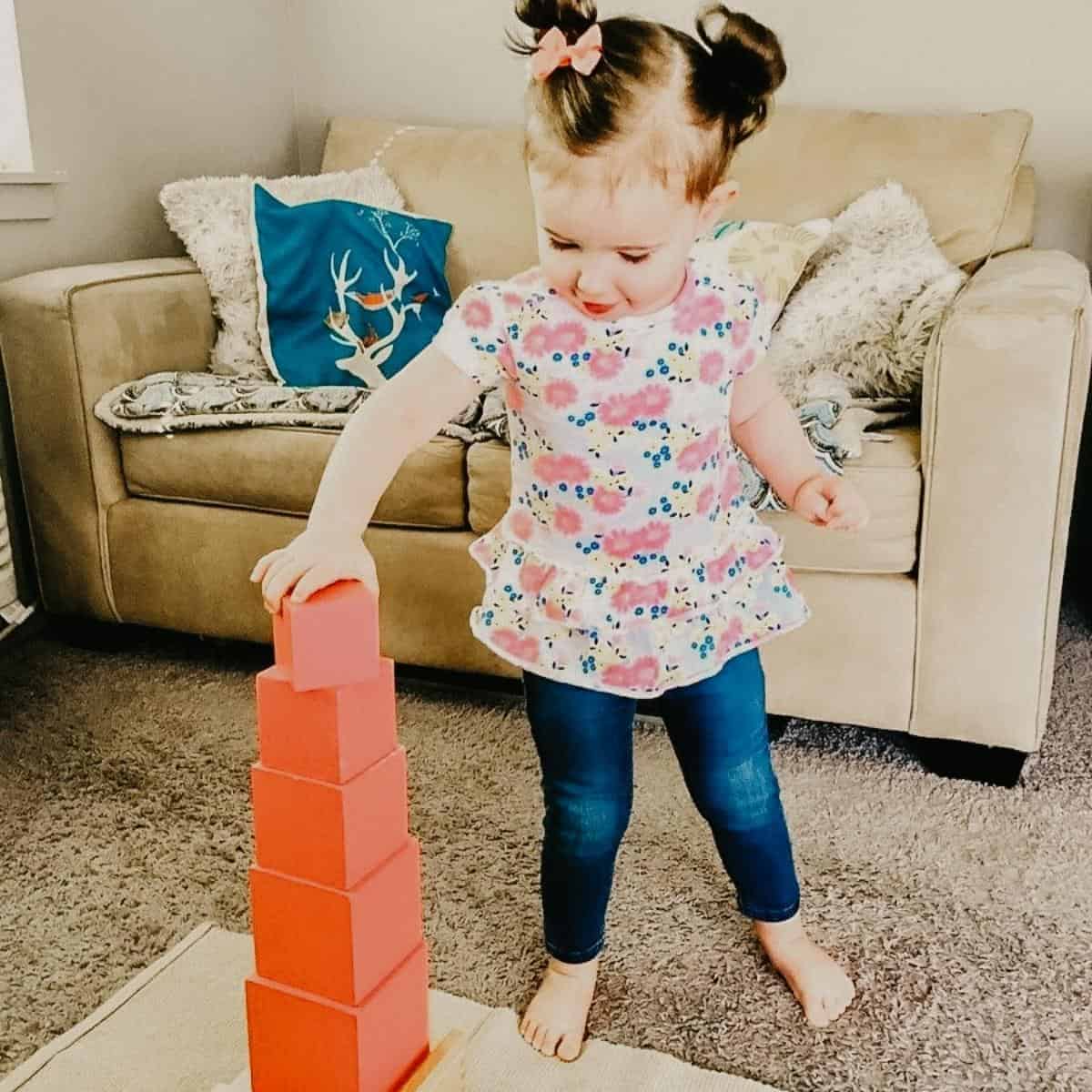 Child building the Montessori Pink Tower on mat in homeschool