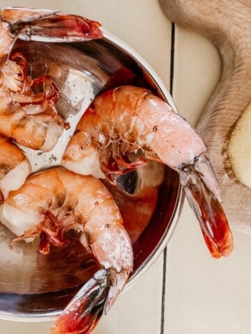 BBQ Prawns in a bowl next to a cutting board and lemon wedge