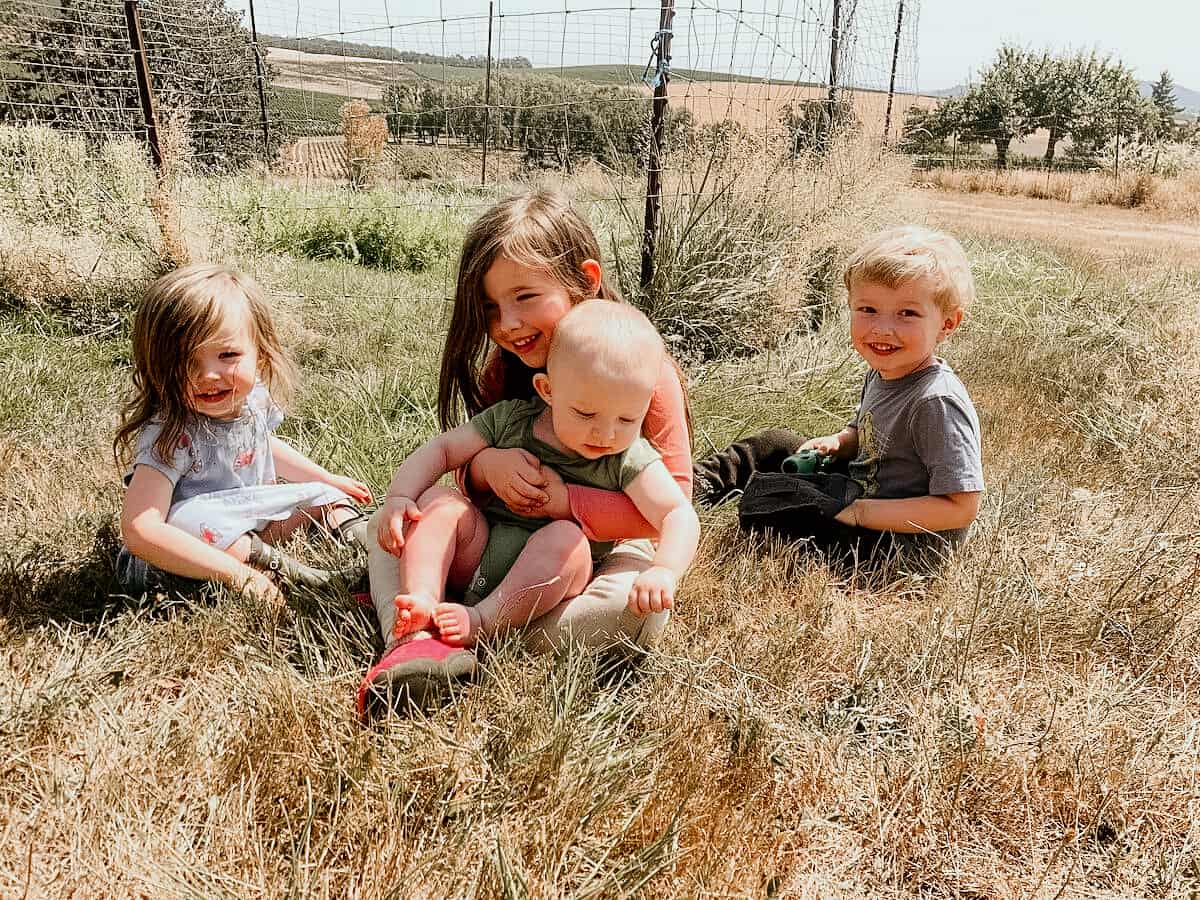 4 kids sitting together in the grass on a farm