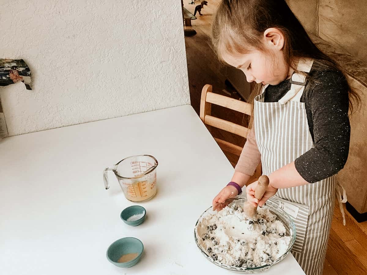 Montessori child stirring blueberry  cake mixture with wooden spoon