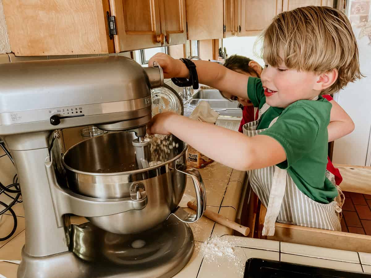 child in a learning tower adding flour to a stand mixer