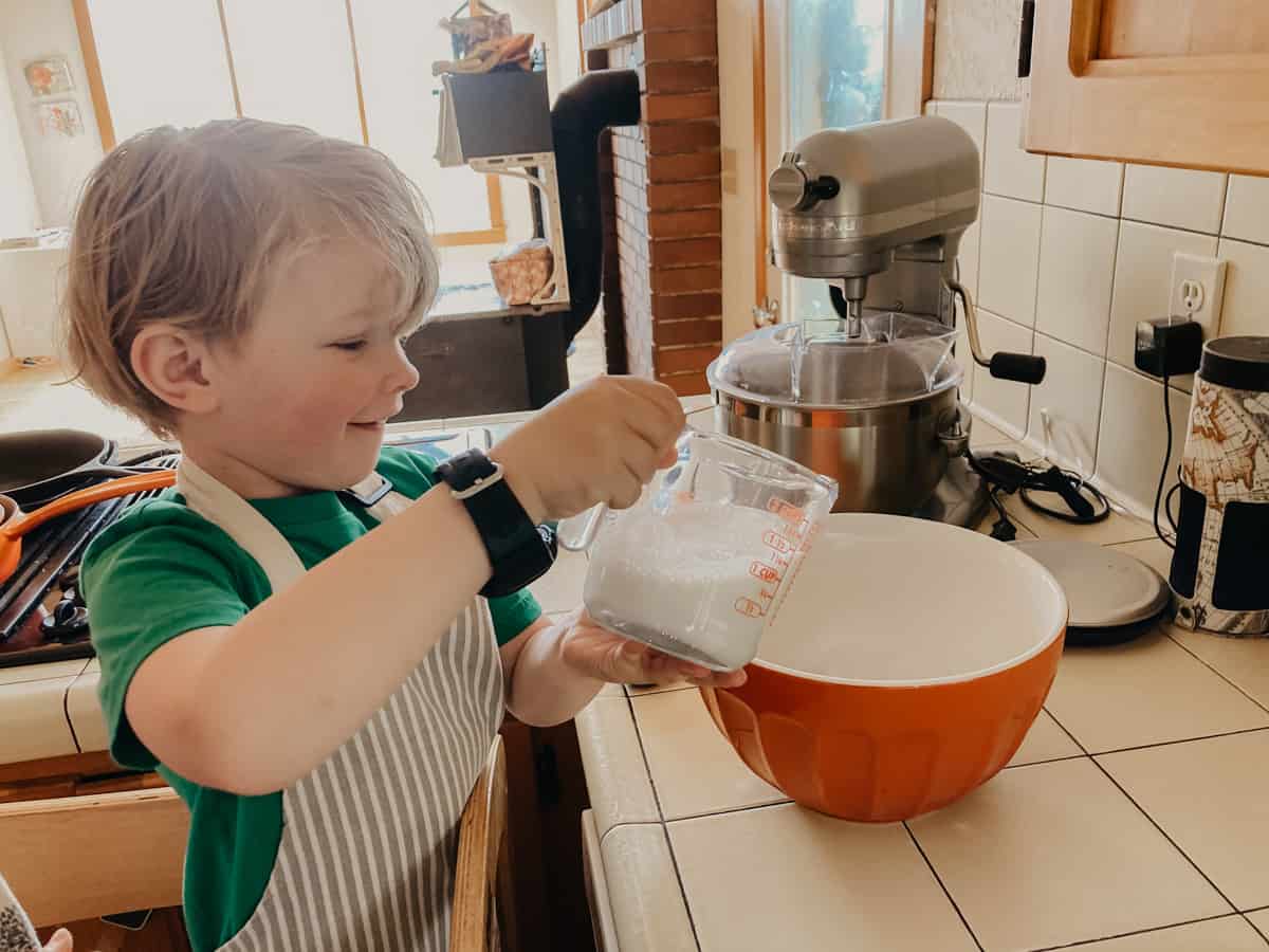 a child adding milk to a bowl with a measuring cup