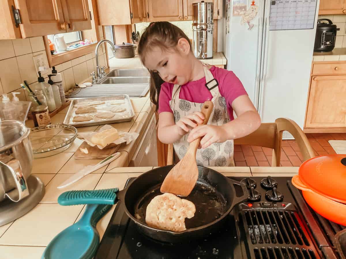 a child at the stove lifting up a bannock with a spatula