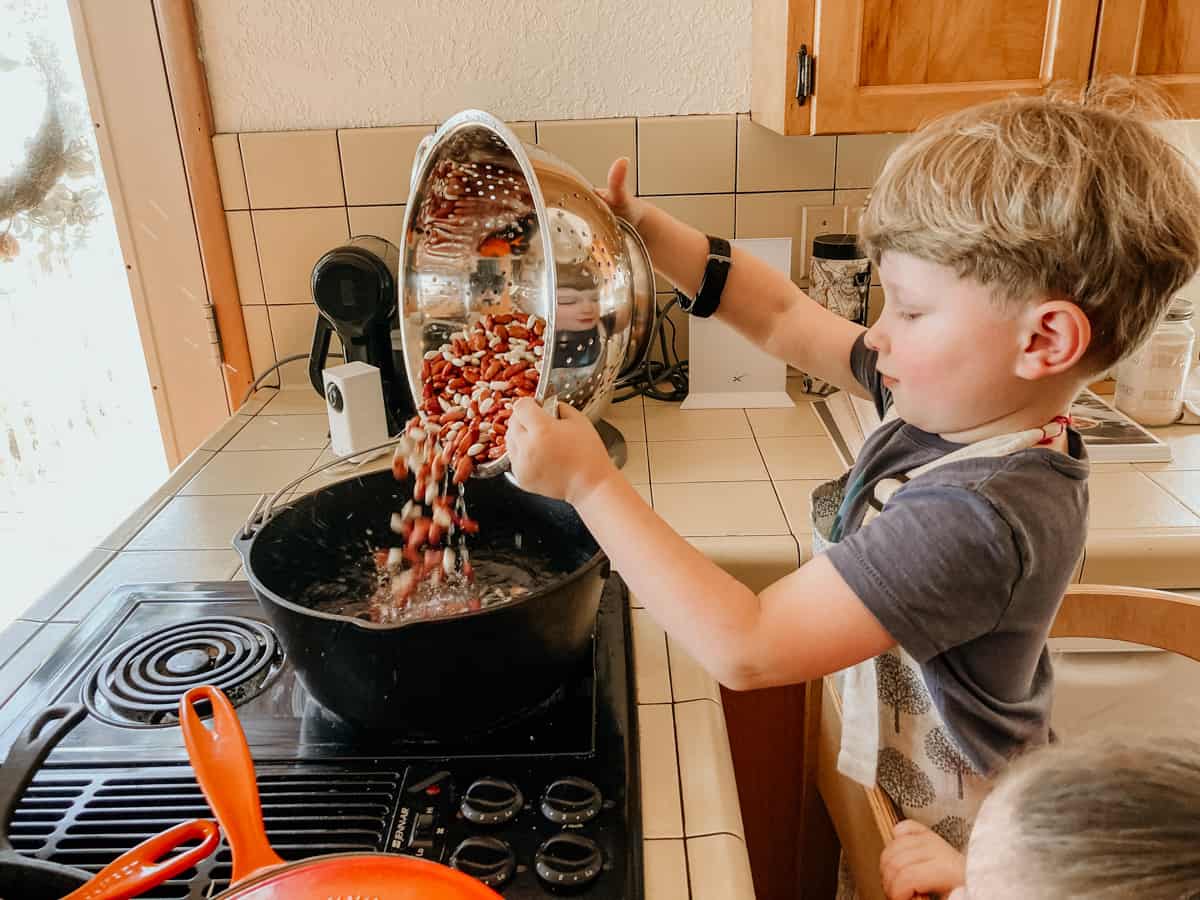 child adding kidney beans and cannellini beans to a large dutch oven containing water