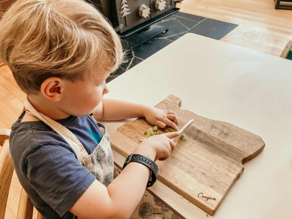 child sitting at a table and chopping celery with a knife and cutting board