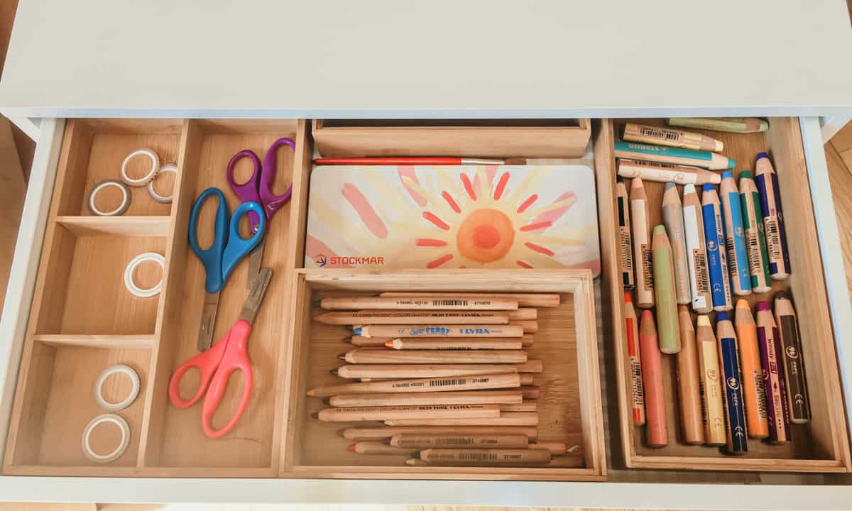 washi tape, scissors, watercolor paints, paintbrushes, colored pencils, and watercolor crayons in trays inside a home art cabinet