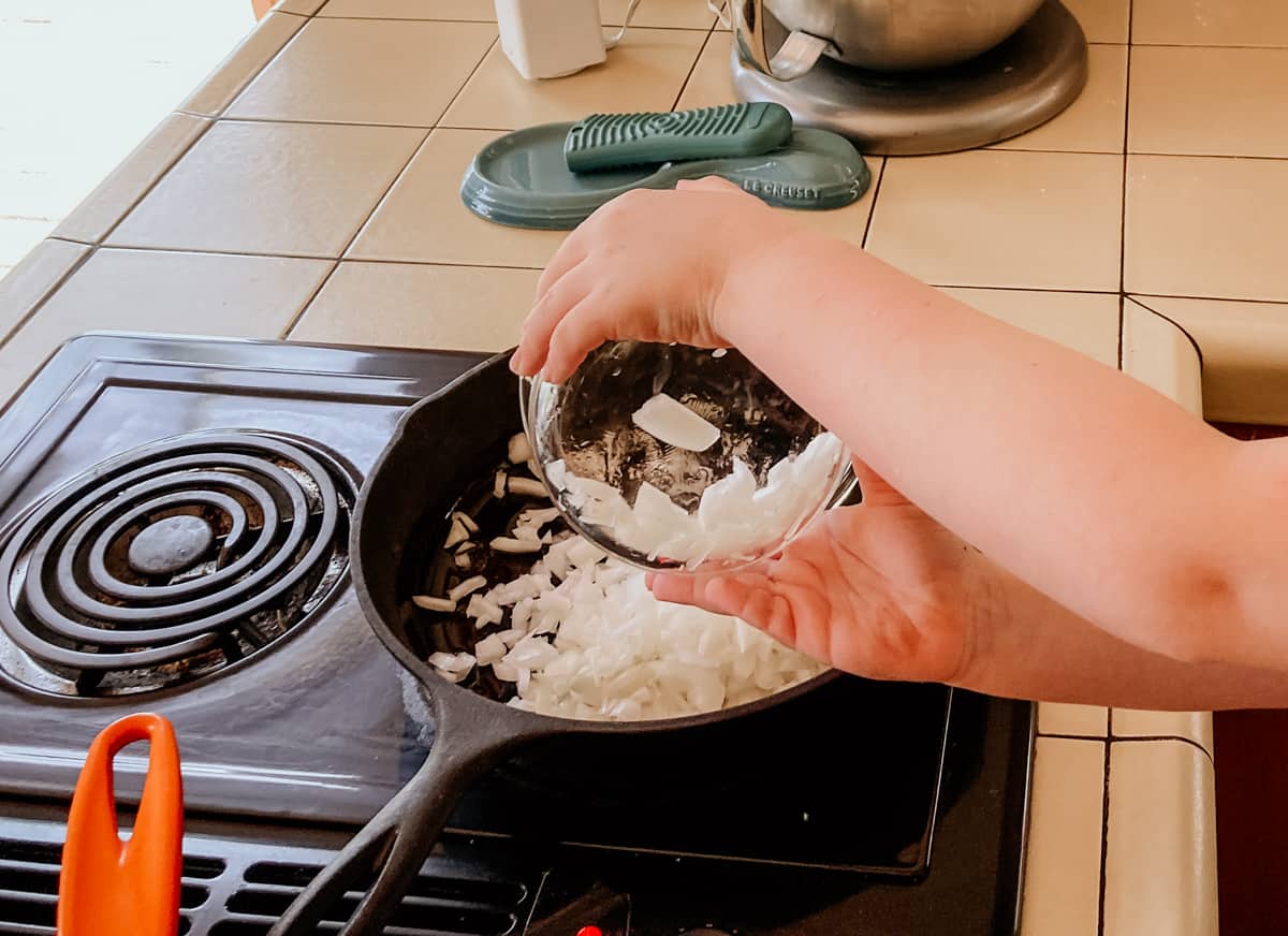 child adding onions to a pan