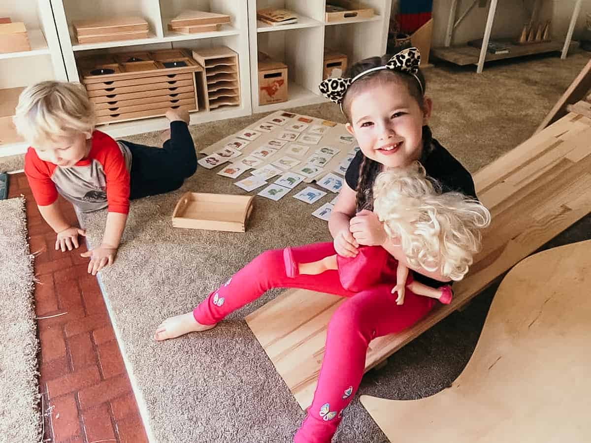 Montessori child holding doll and sitting on an indoor slide next to another child on the floor