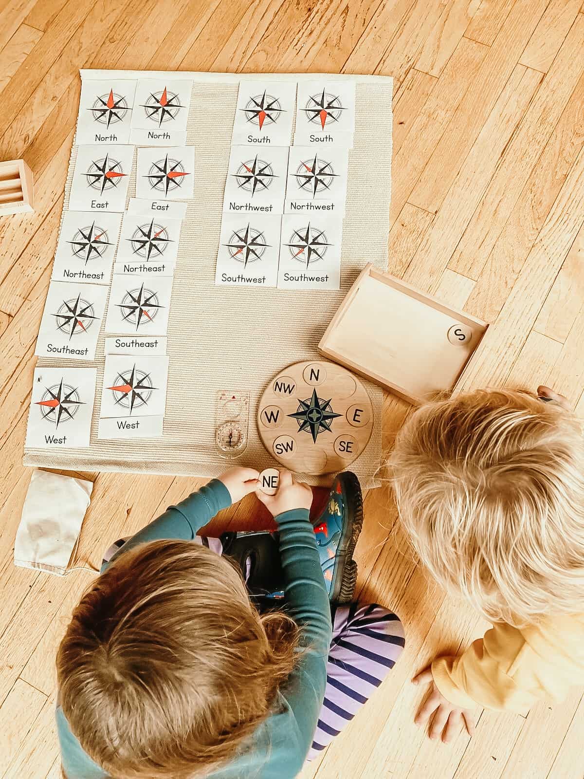 compass rose puzzle and cards lying on a mat next to children