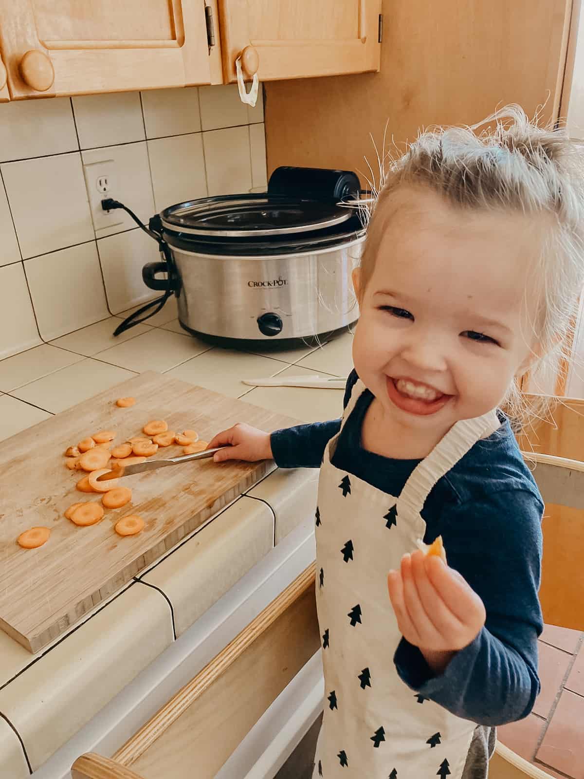 child smiling and eating carrots with an apron on