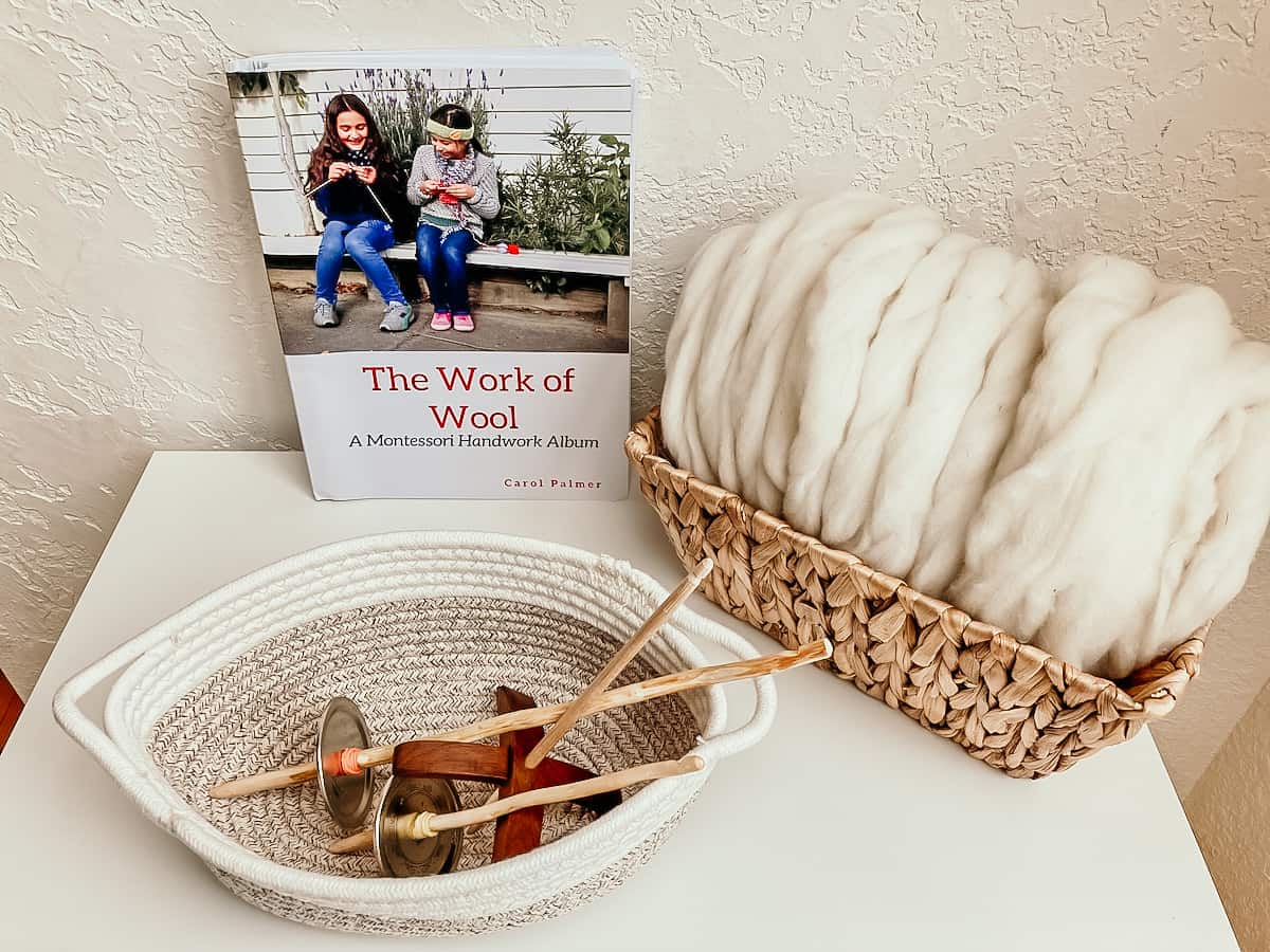 The Work of Wool book, wooden spindles in a basket and sheep roving in a basket