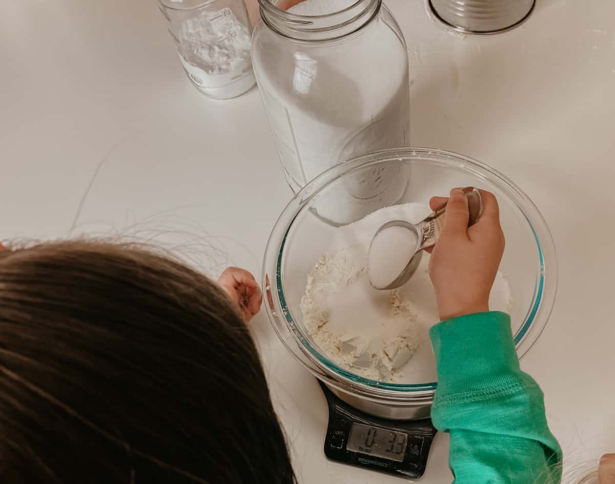 child adding stevia to a bowl of ingredients on a kitchen scale