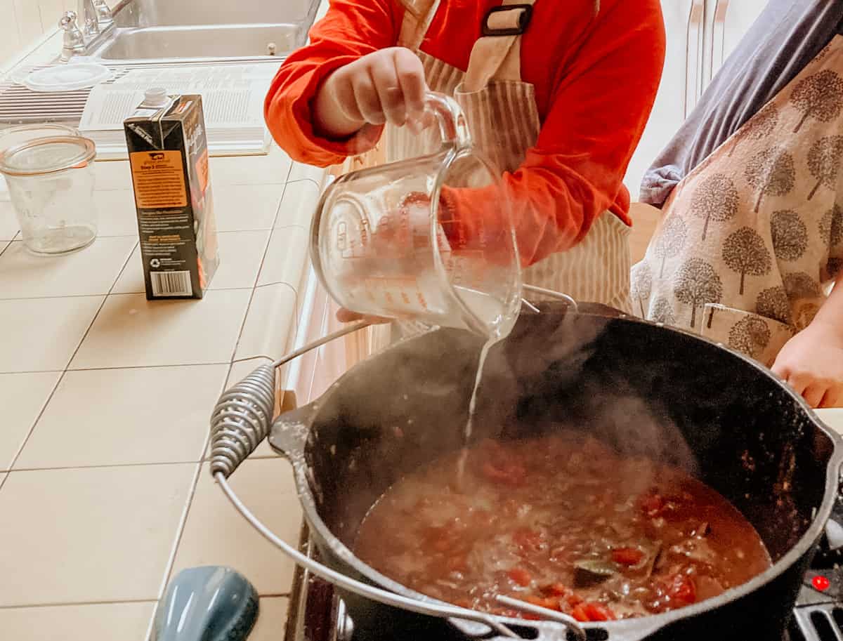 a child is pouring chicken stock into a dutch oven 