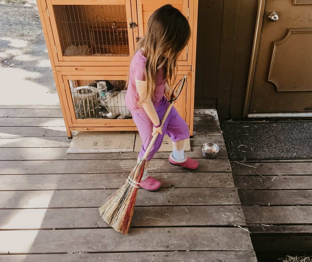 child sweeping the back deck with a rainbow broom