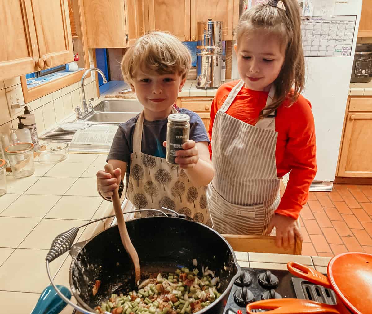 child holding a bottle of thyme over a dutch oven with ingredients for making rabbit stew