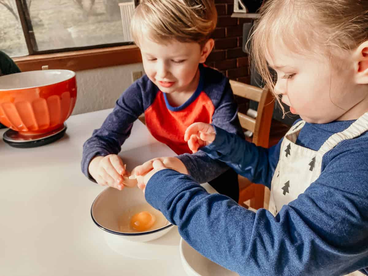 kids cracking eggs into a bowl
