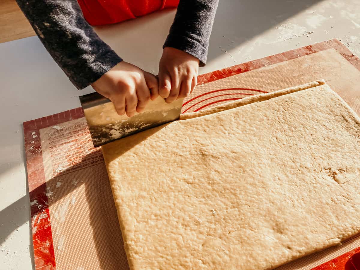 child using a dough scraper to cut a slice of dough for making mallorcas