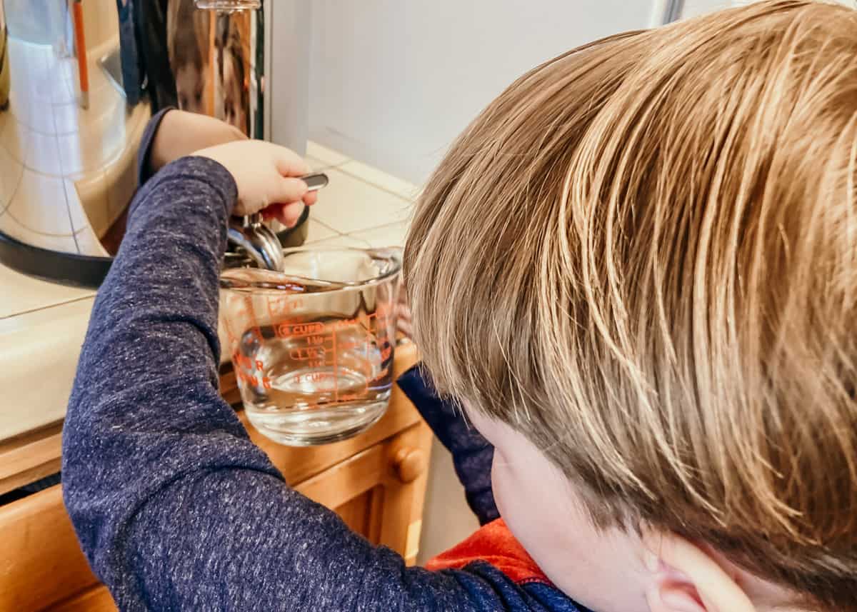 child filling a measuring cup with water from a Berkey