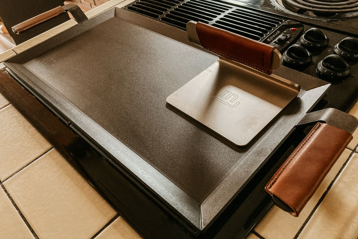 closeup of a carbon steel griddle and grill press on a kitchen stove