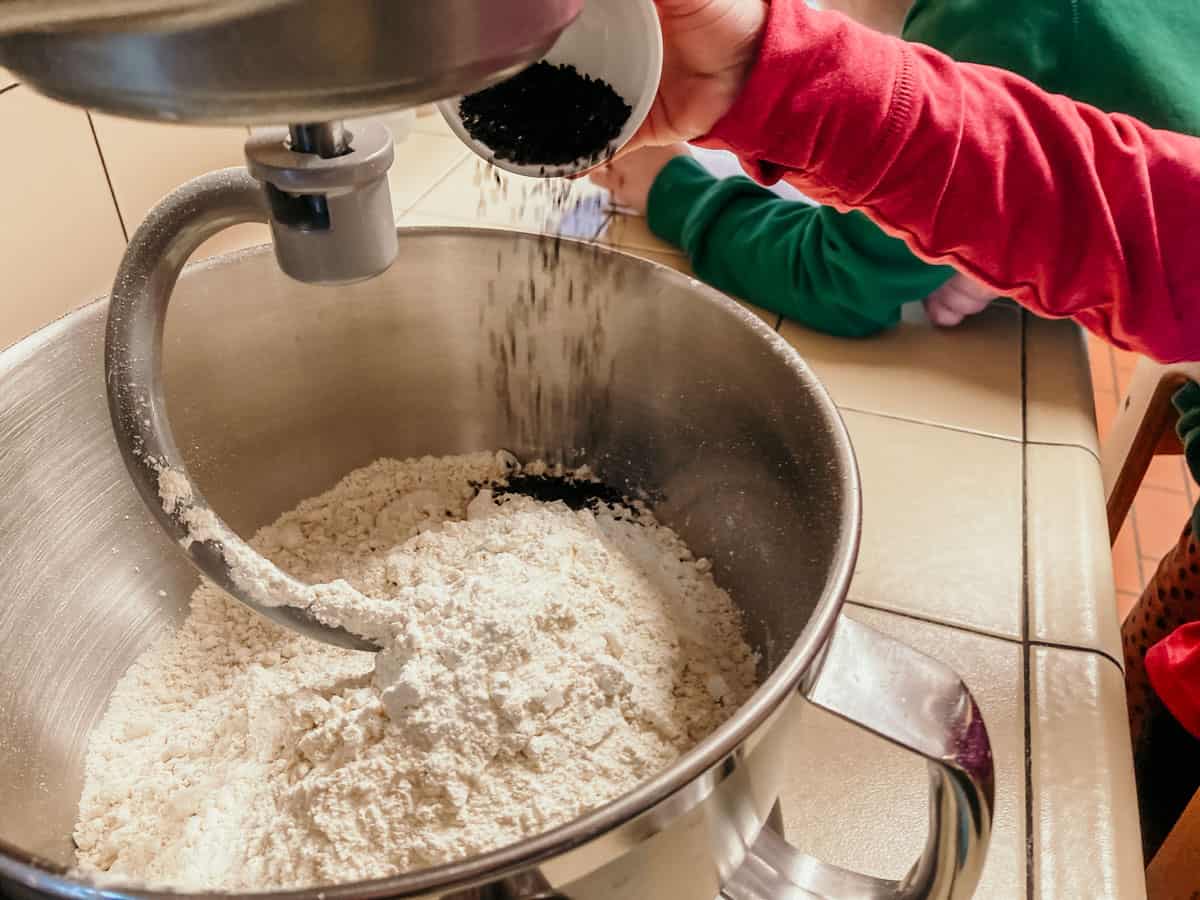 closeup of a child adding nigella seeds to a mixing bowl with flour