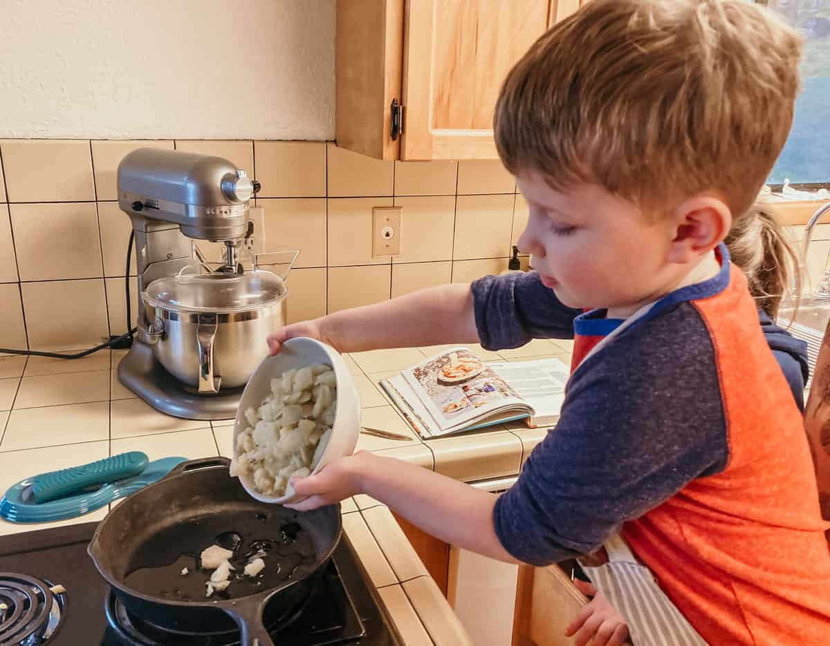 child pouring a bowl of cubed potato into a cast iron skillet