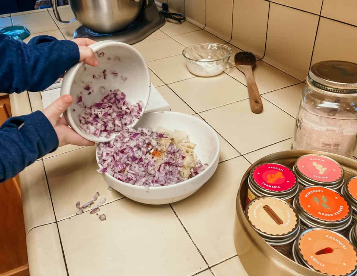 closeup of a child pouring a bowl of red onion into a bowl of ingredients