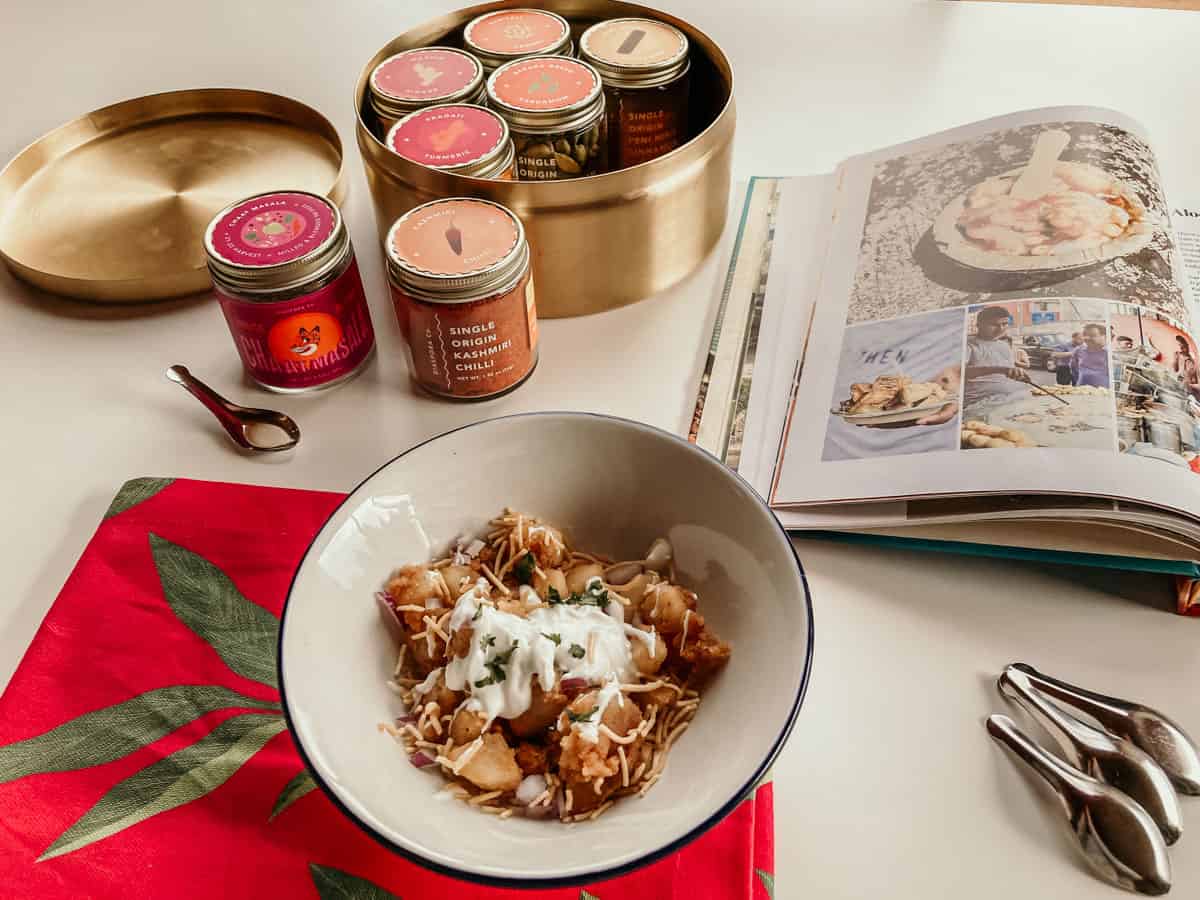 A bowl of Aloo Chaat next to Chaat cookbook, Diaspora Co. spices, and a spice spoon
