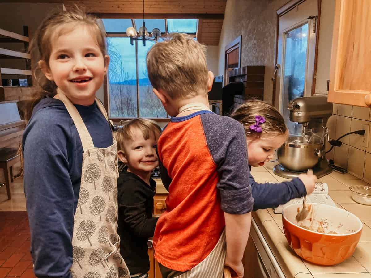 four kids standing in a learning tower in the kitchen