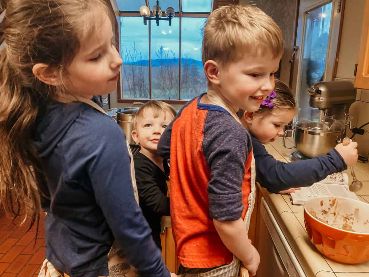 four kids standing in a learning tower in the kitchen