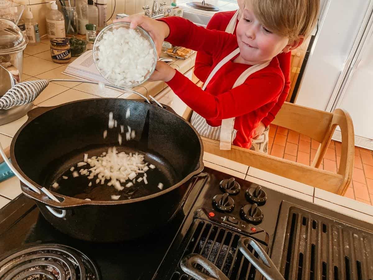 child pouring onion into a dutch oven