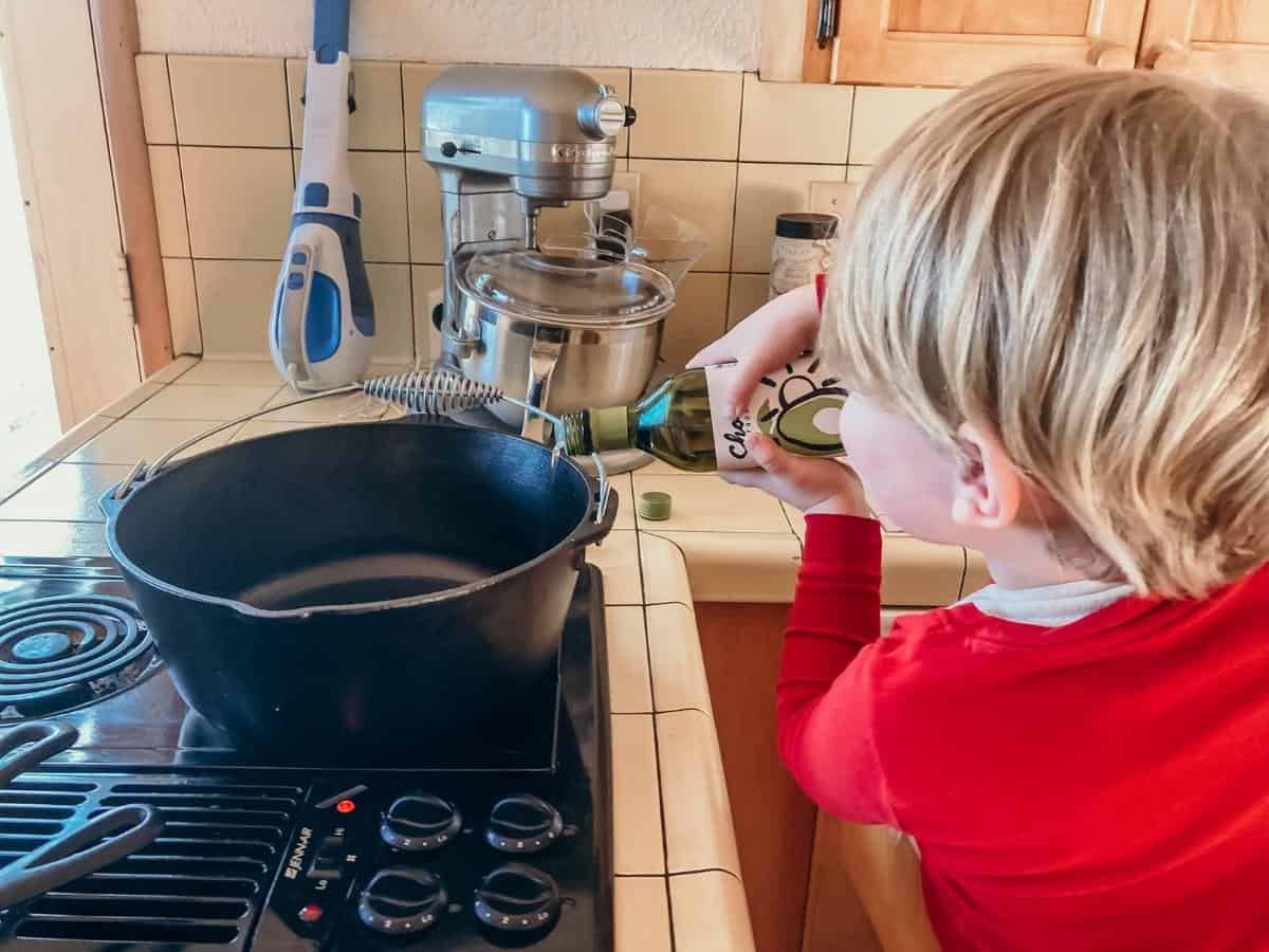 child adding avocado oil to a dutch oven