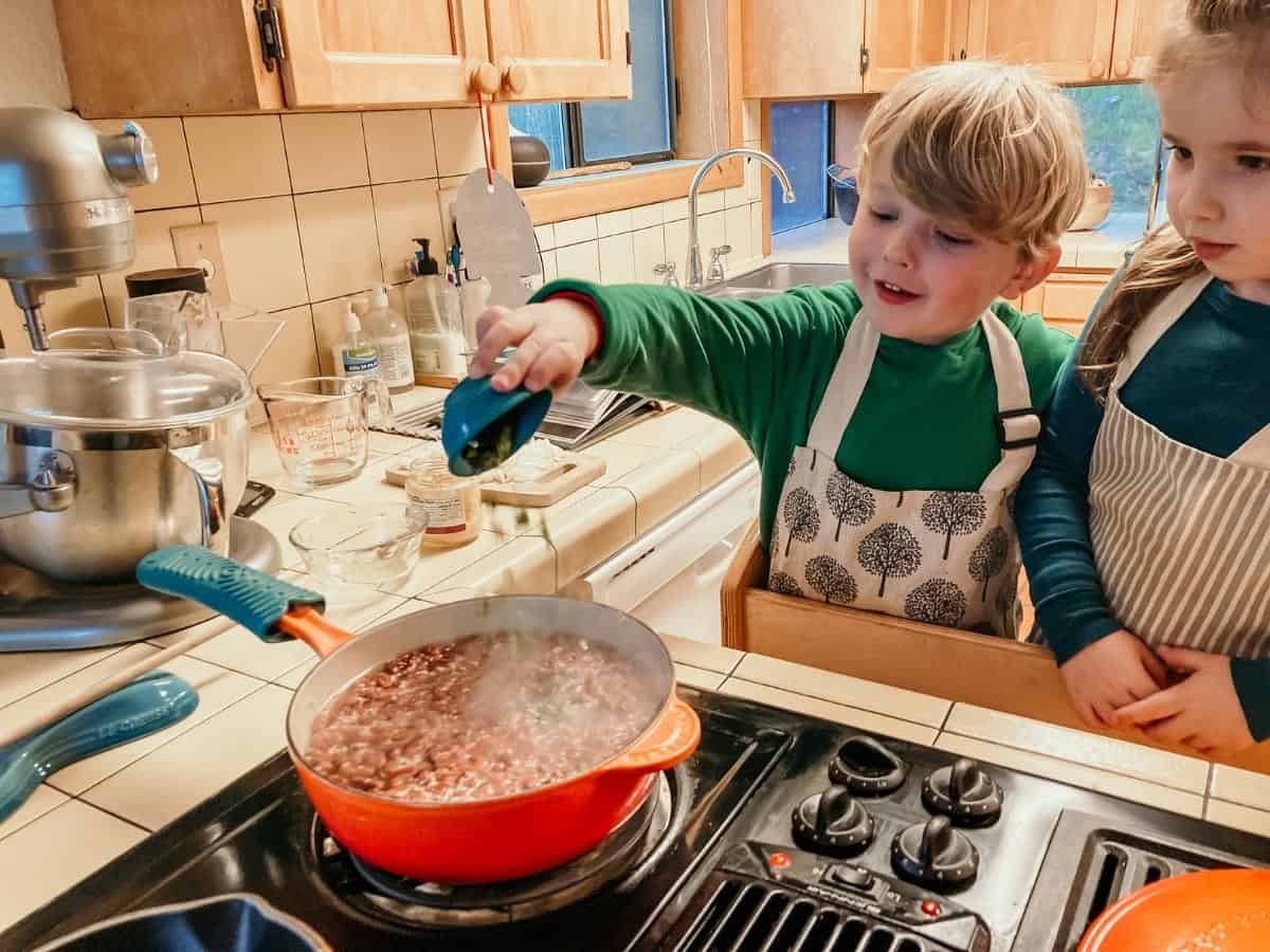 child adding chile to saucepan of ingredients