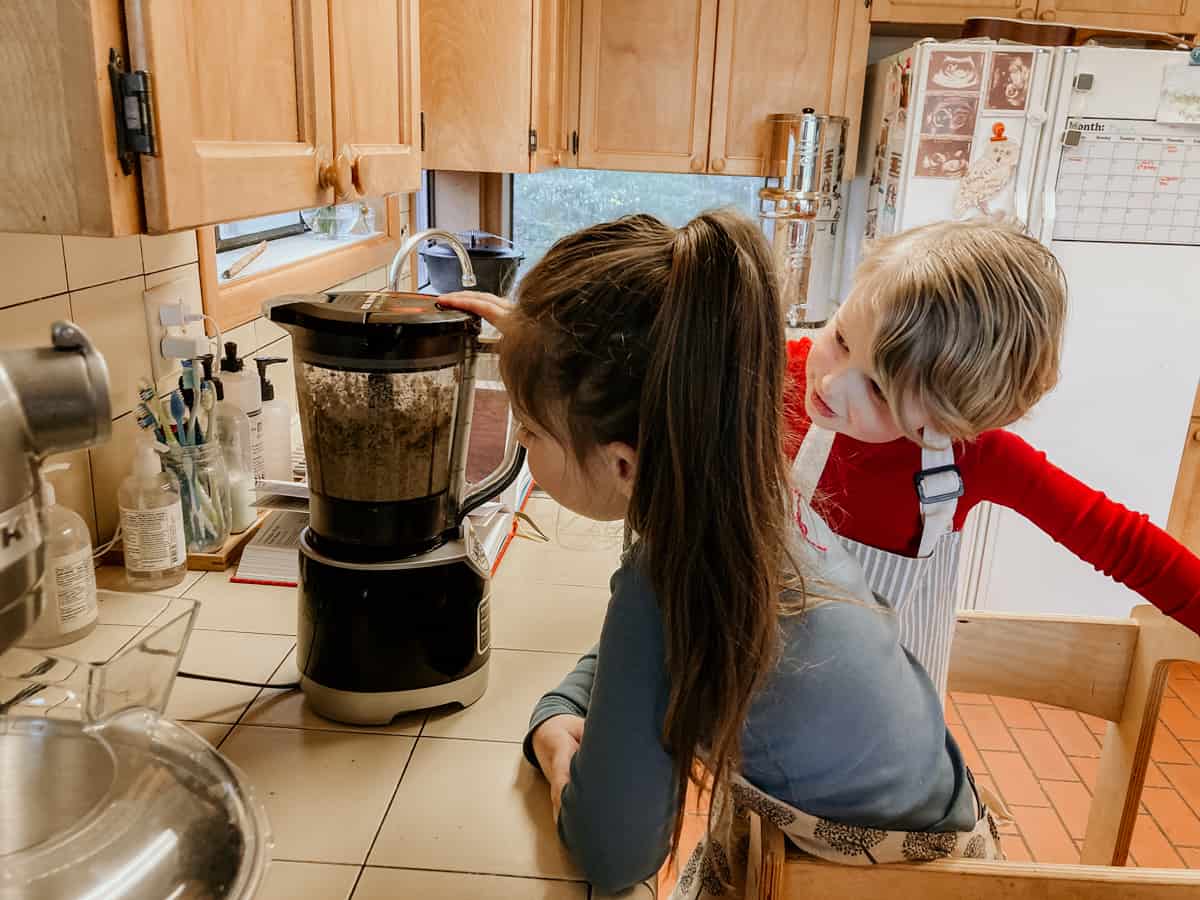 two kids are watching a blender combine ingredients