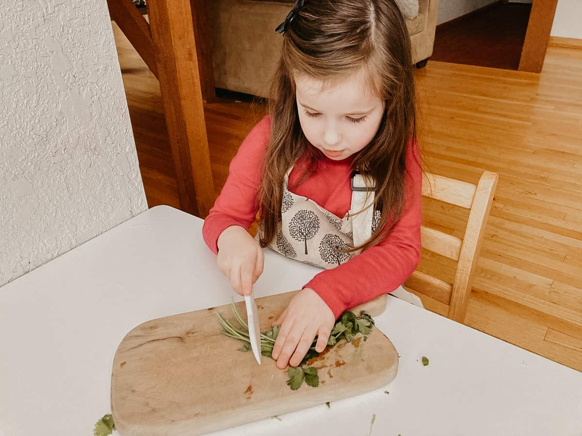 a child chopping cilantro on a cutting board with a knife 