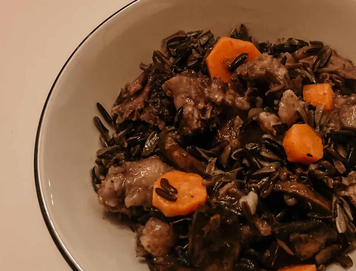 closeup of a bowl of braised oxtails, black rice, and vegetables