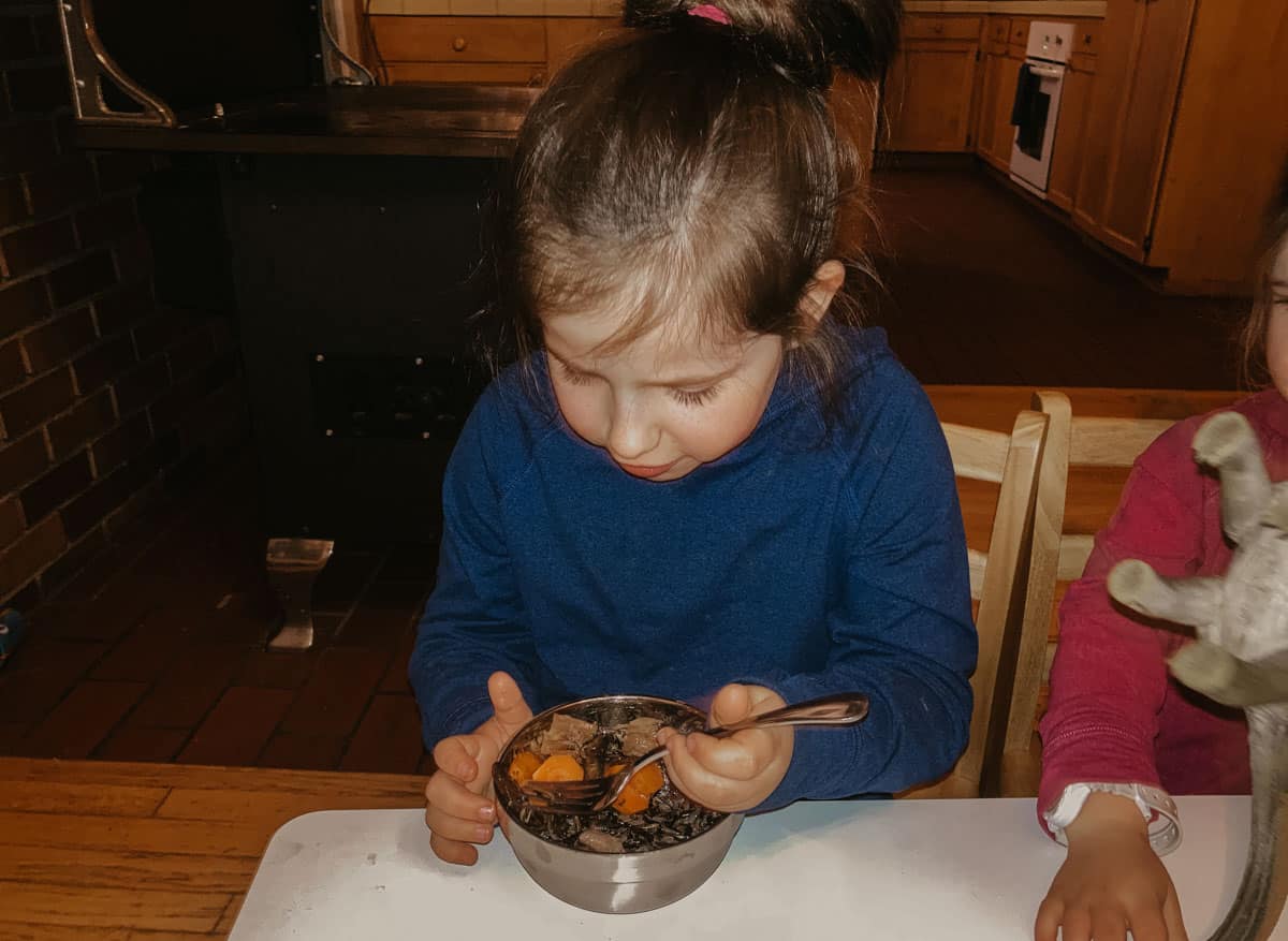 child eating a bowl of braised oxtails, black rice, sauteed mushrooms, and roasted carrots