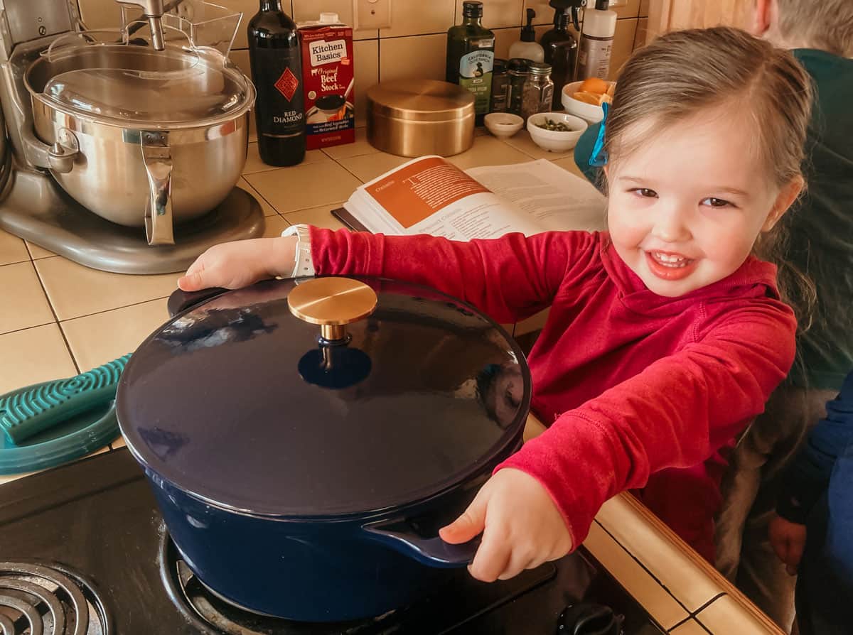 child holding the handles of a dutch oven