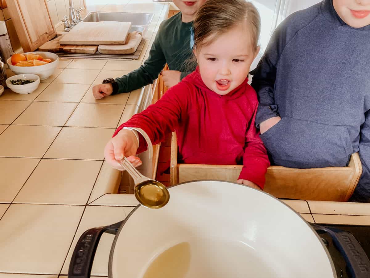child adding olive oil to a dutch oven using a measuring spoon