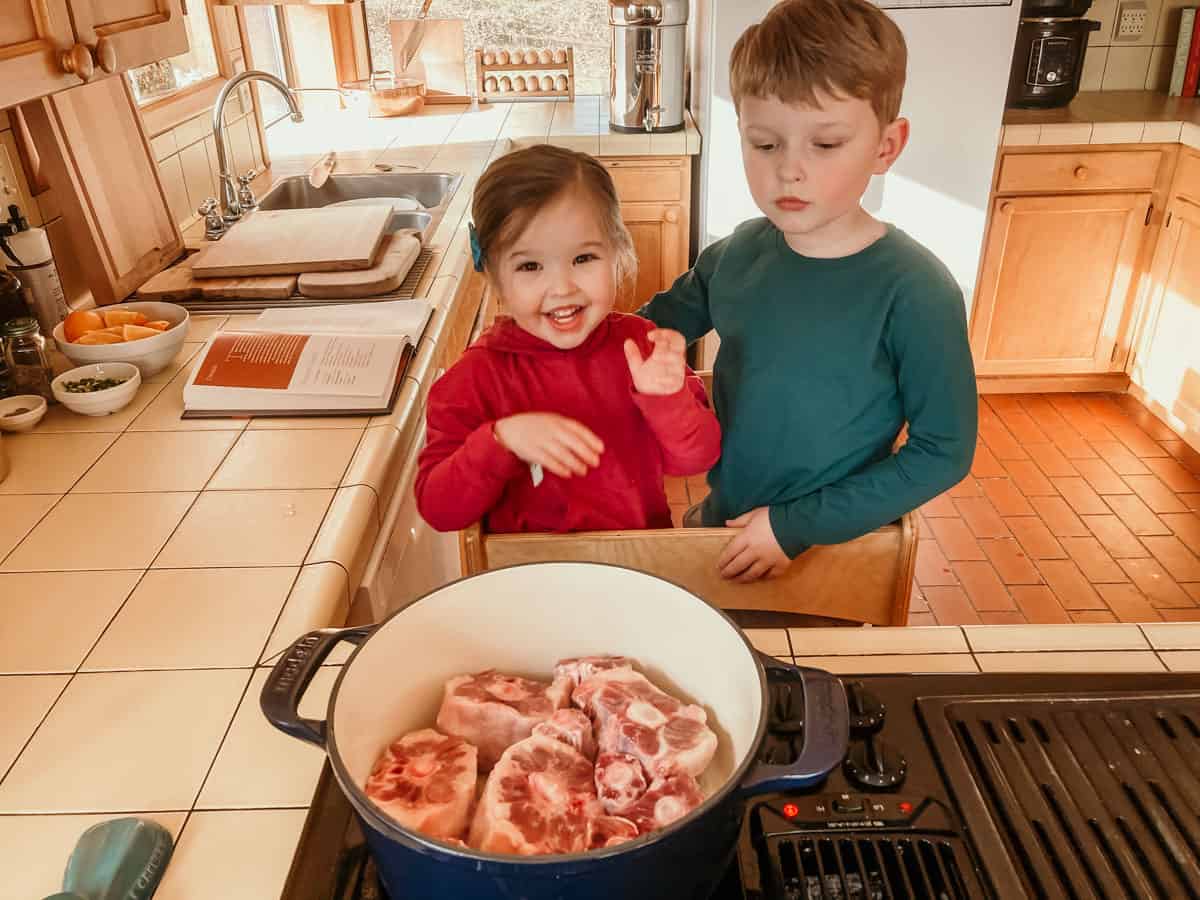 kids standing in a learning tower at the stove. In front of them is a dutch oven with oxtails inside