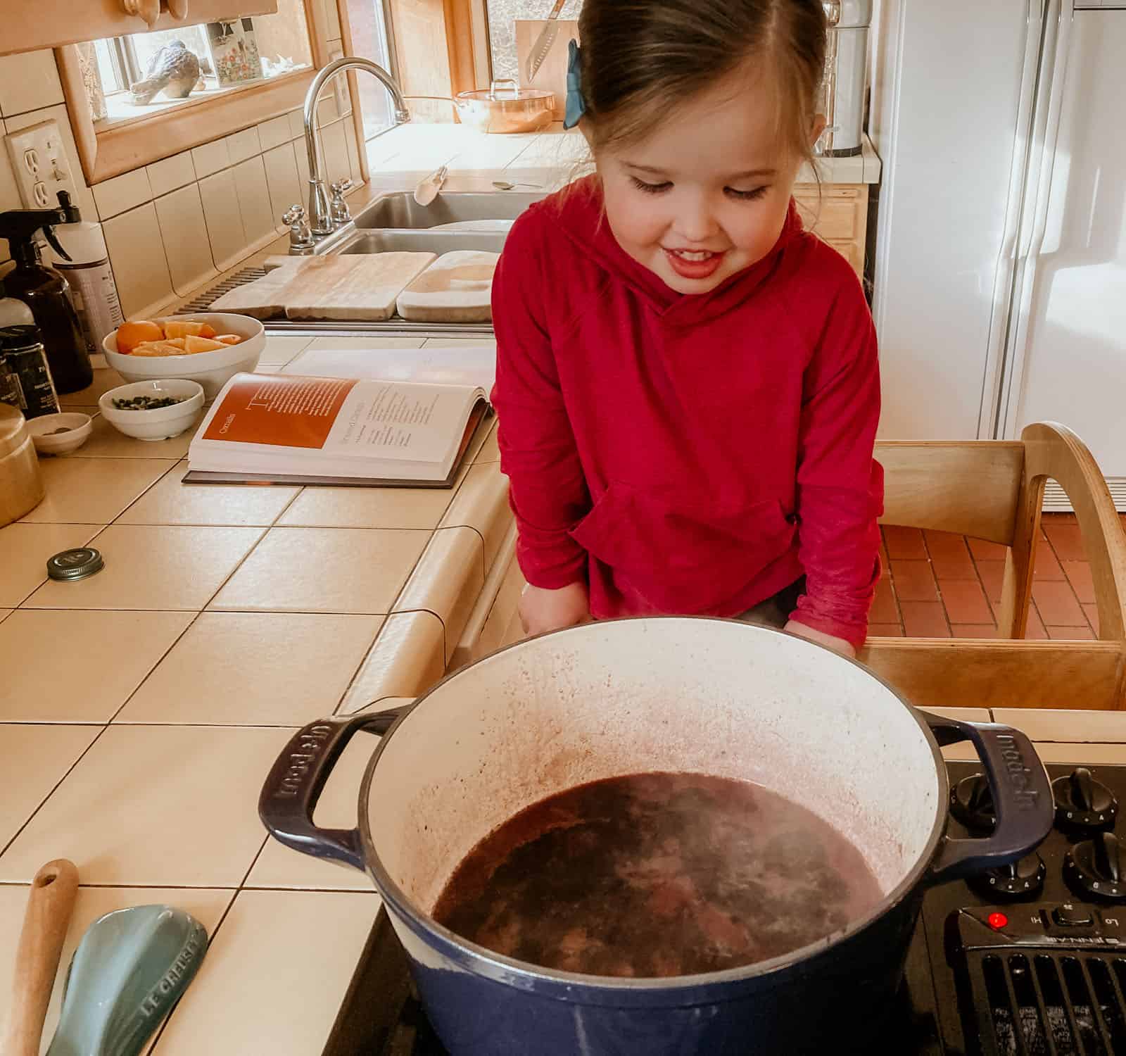 child standing in a learning tower over a dutch oven with ingredients