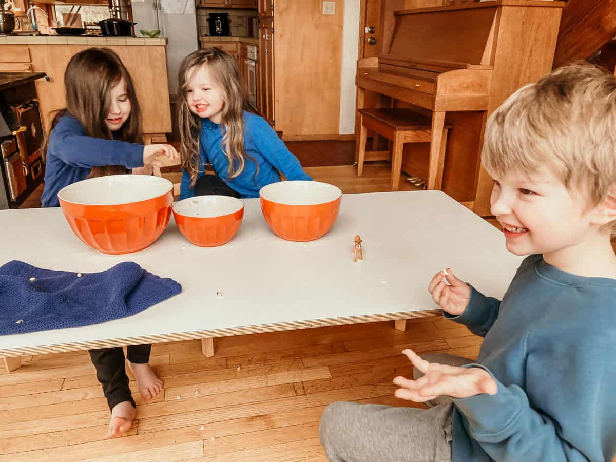 three kids sitting at a kids' table peeling black-eyed peas and laughing