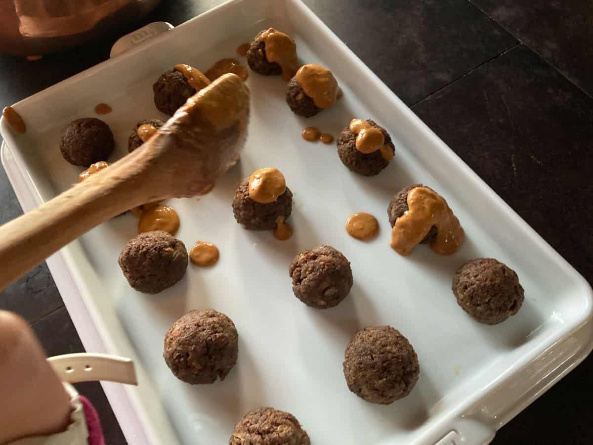 closeup of child spooning West African peanut sauce onto bison meatballs on a Made In Baking Slab