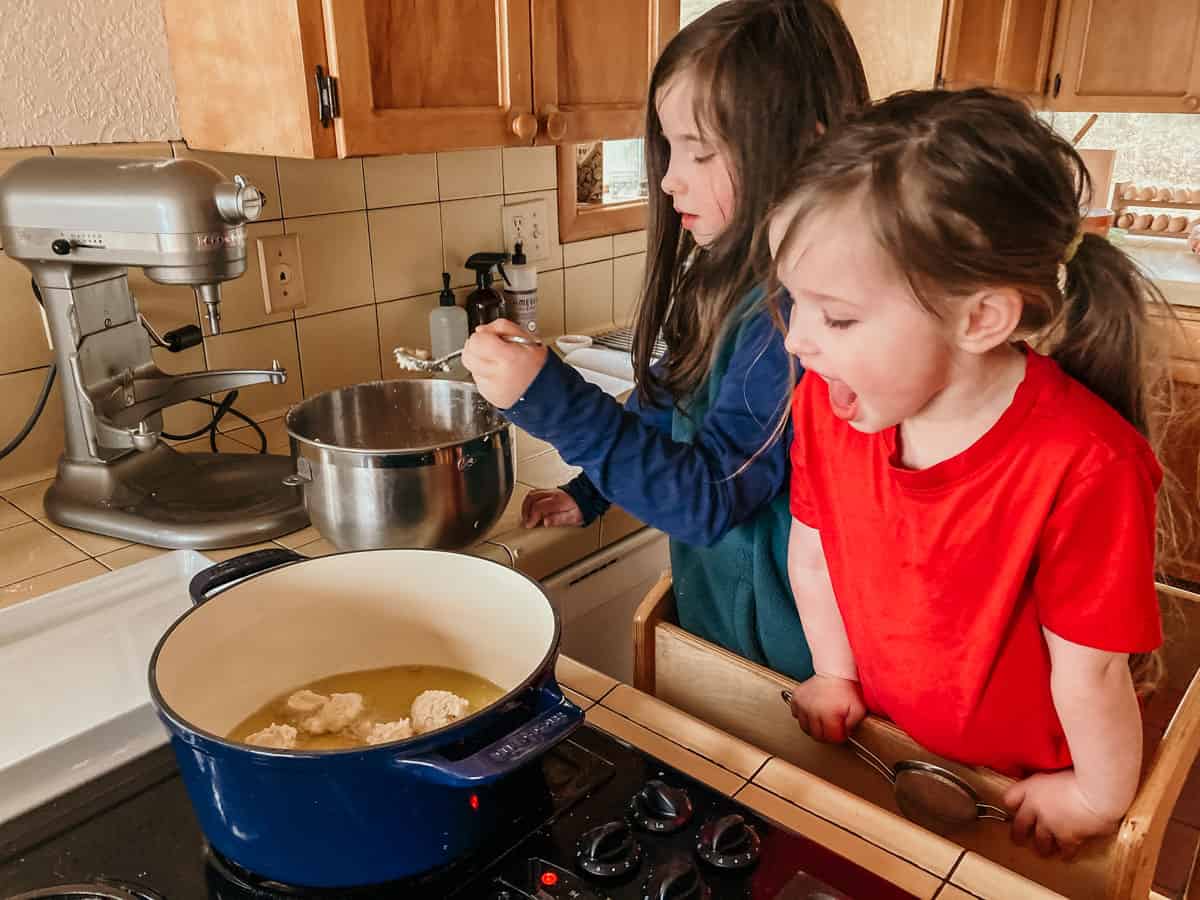 kids standing in a learning tower at the stove and one child is excited to watch the black-eyed pea puffs frying in the oil